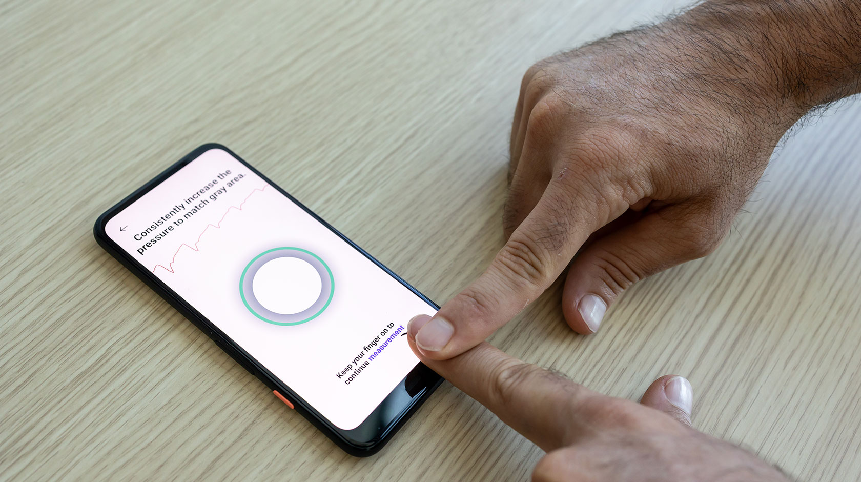 A person uses one pointer finger to press their other pointer finger onto the screen of a smartphone. The screen has text instructions of how to take a blood pressure reading.