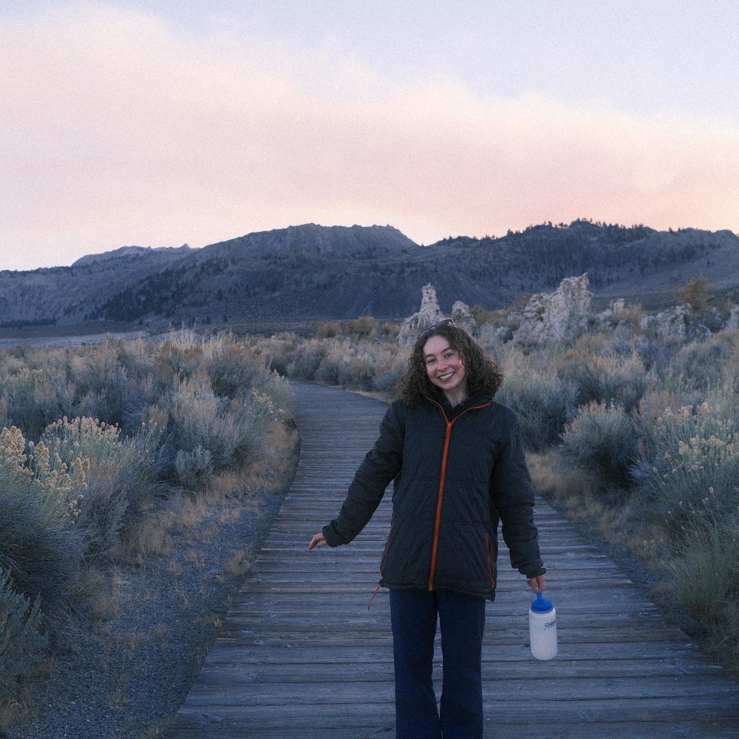 Allie Larman on a wooden walkway near Mono Lake at sunset, smiling, holding a water bottle