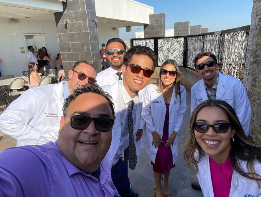 Six young people in white coats gather for a selfie, taken by Marco Angulo, in the lower left corner. All wear sunglasses.