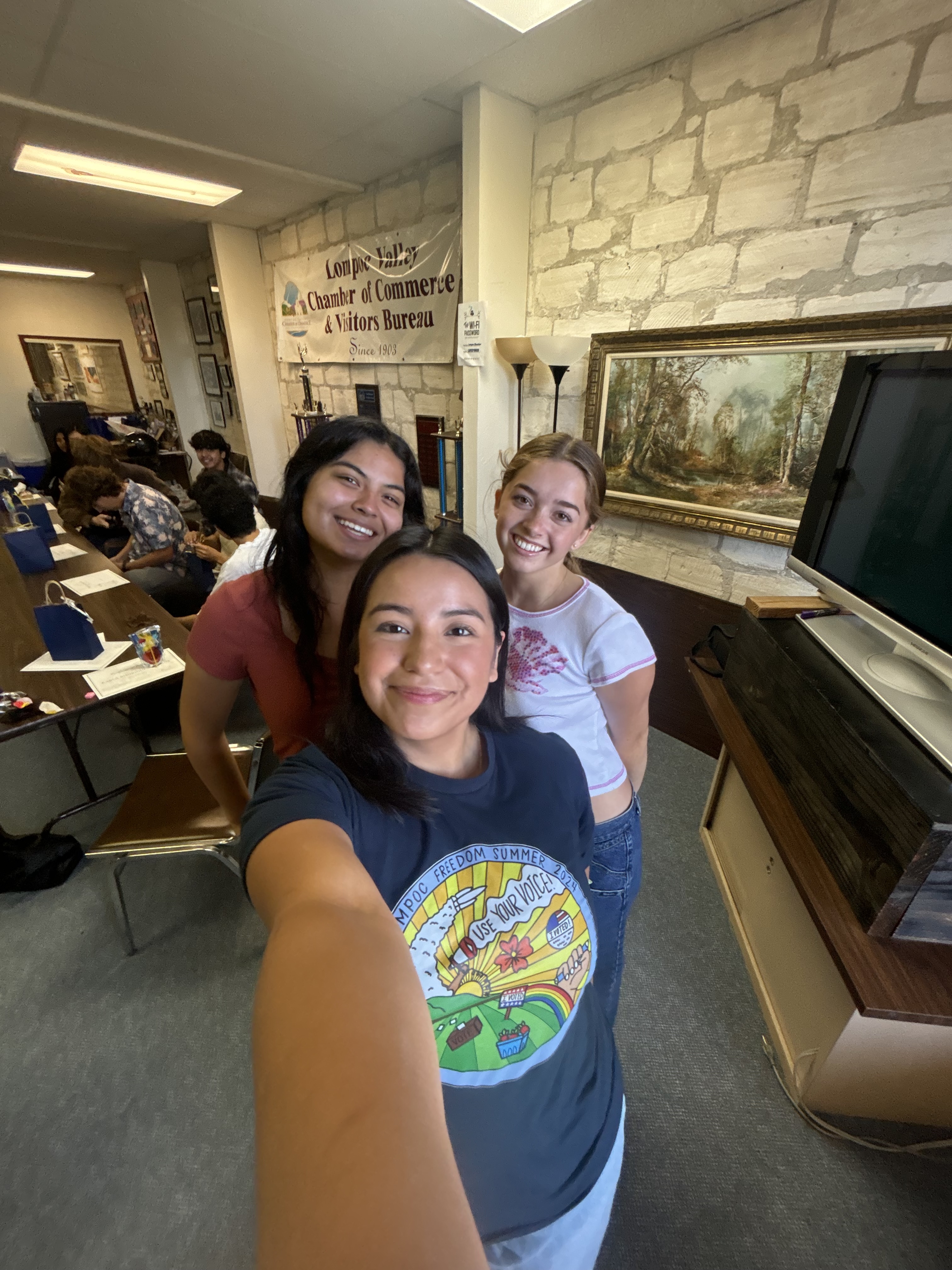 Three young women smile for a selfie in the lobby of Lompoc City Hall.