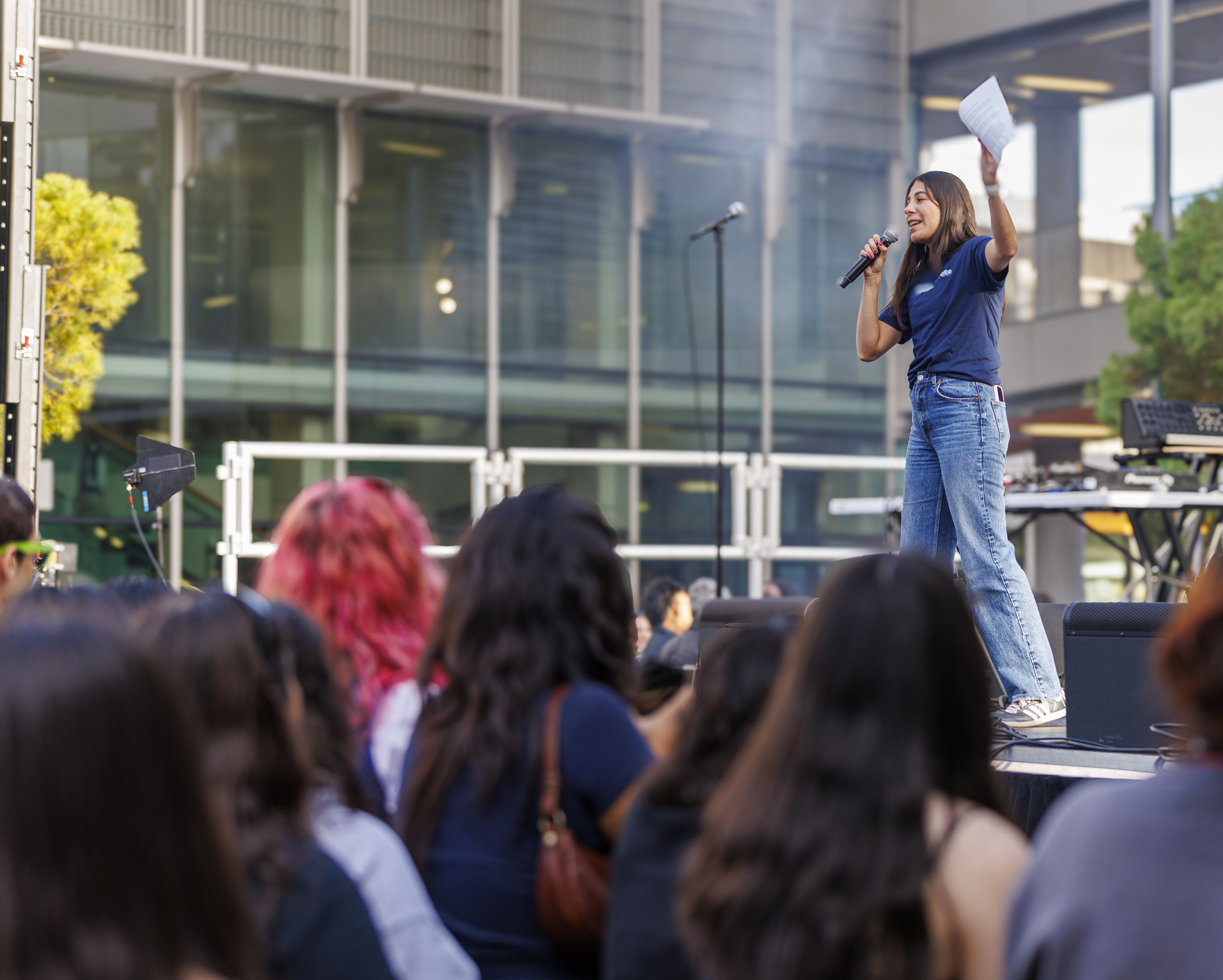 A student wearing a GO BEARS. GO VOTE. t shirt stands on a stage in Sproul Plaza, speaking into a microphone and gesticulating, in front of a crowd