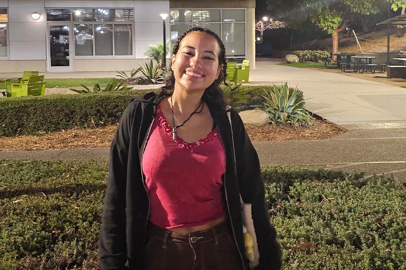 Young woman in tank top and hoodie smiling on campus