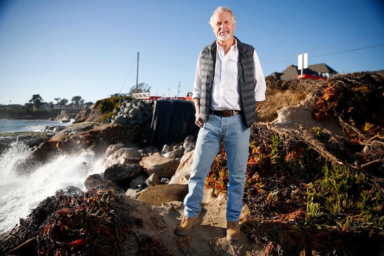 Gary Griggs stands on a rocky coastline, steps away from crashing waves