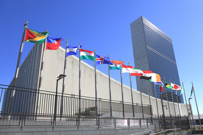 UN Headquarters photographed from street level on a sunny day, the breeze blowing the UN flags 