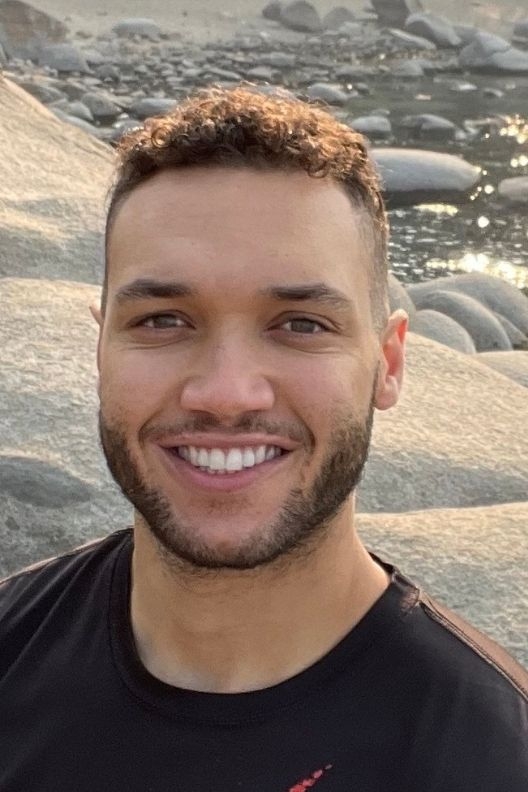 Jordan Garrett smiles at the camera, standing in a field of smooth gray rocks