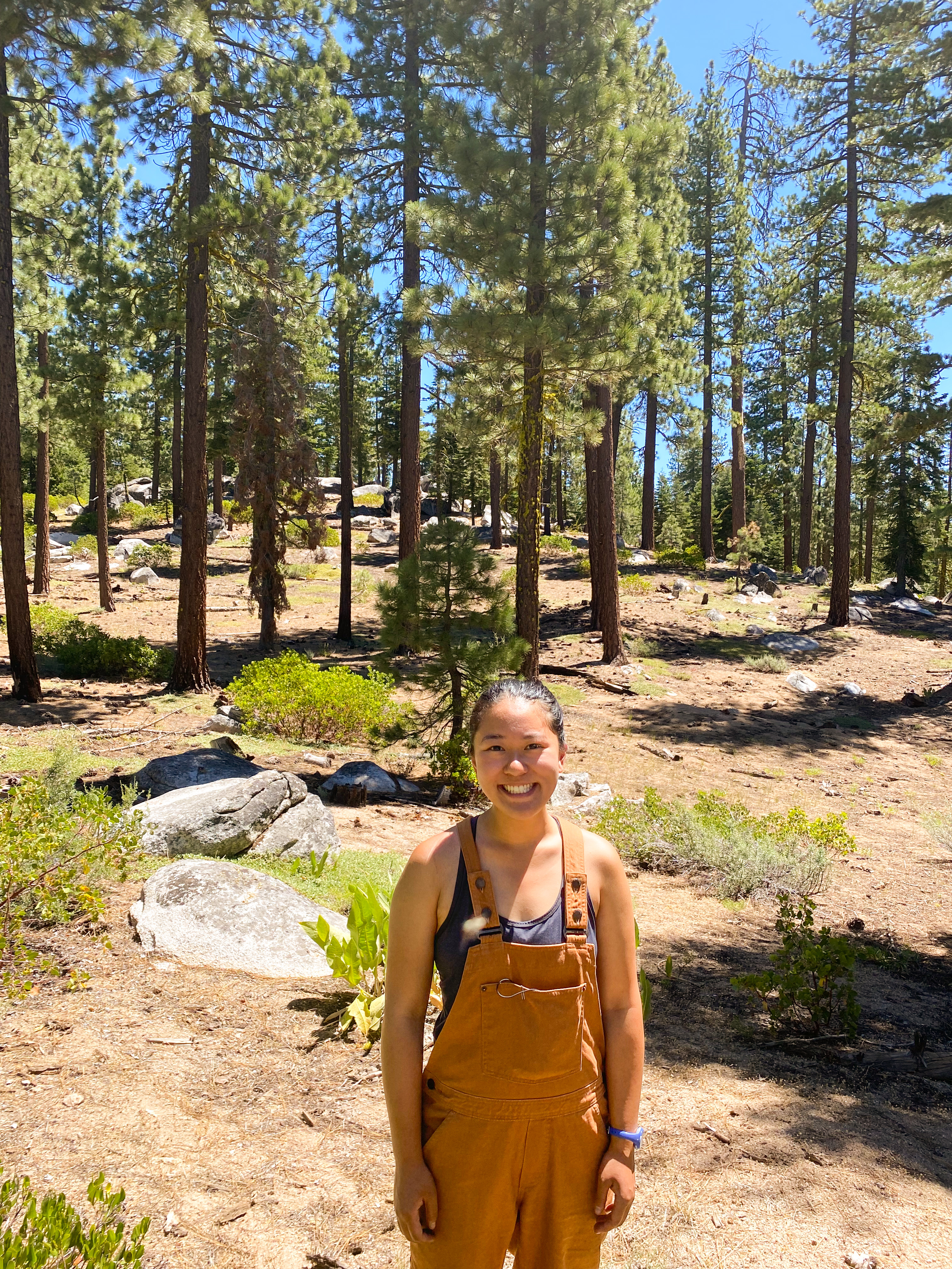 Katie Low wearing overalls stands in a Sierra forest smiling