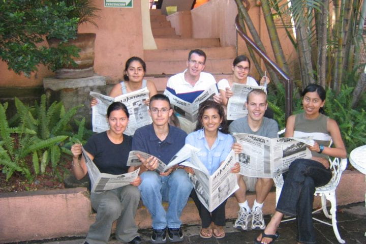 8 students sit on outdoor steps reading newspapers