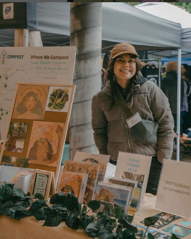 Valeree Catangay smiles at a booth with her art displayed in front of it