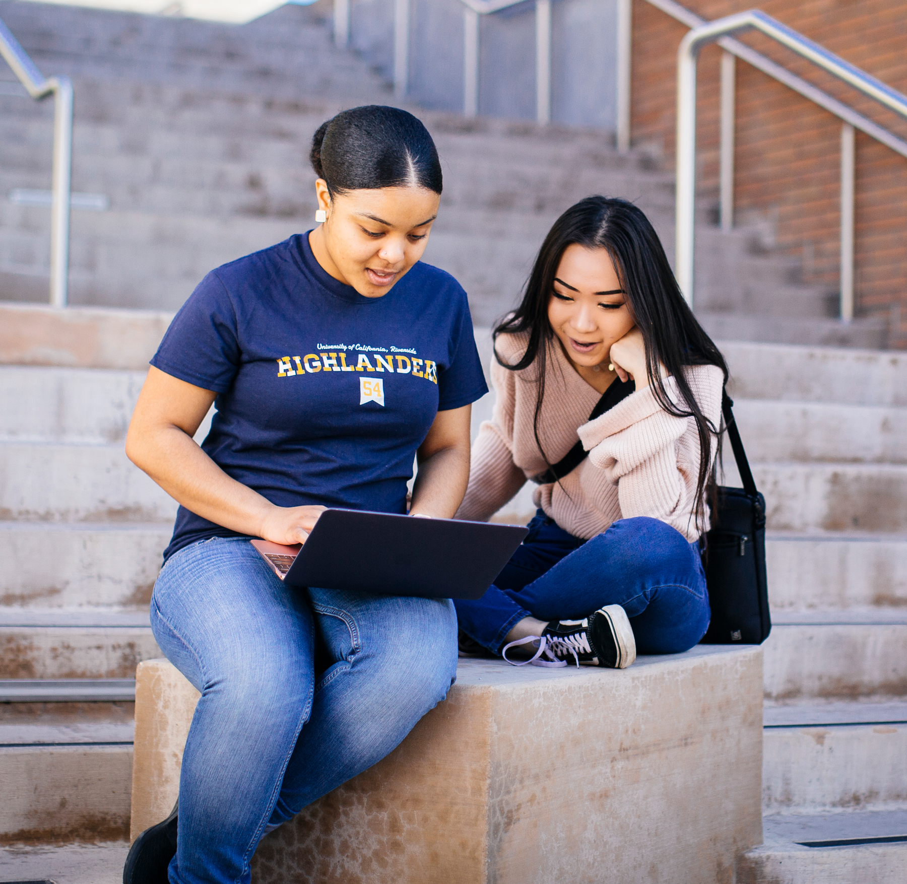 Two students sitting on an outdoor staircase looking at an open laptop