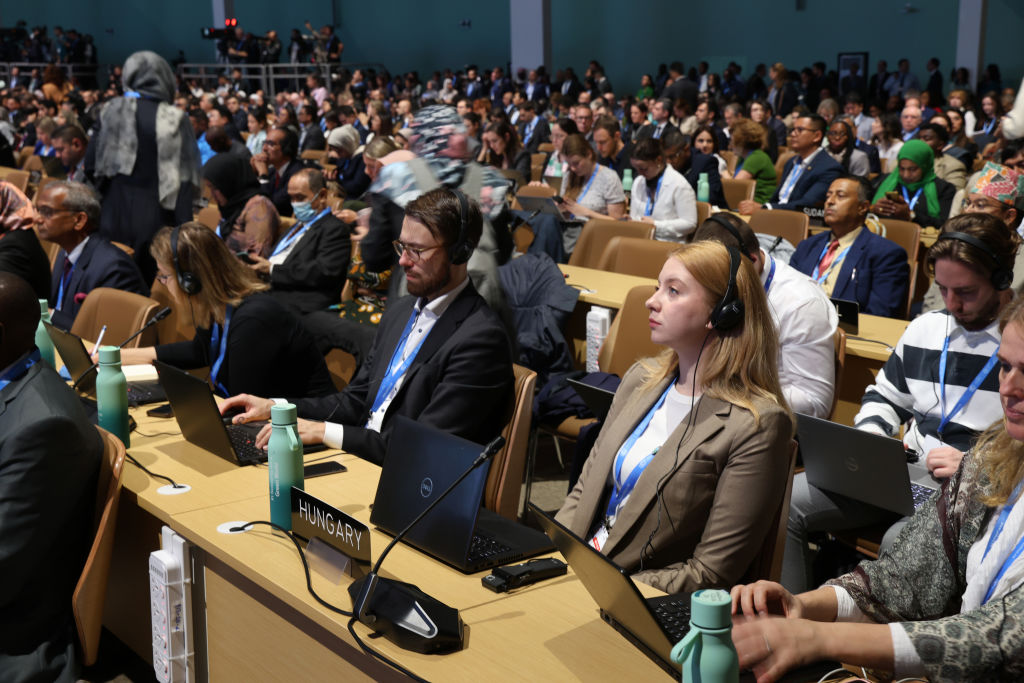 A room full of people sit at desks facing the front of the room, all wearing headsets to translate languages