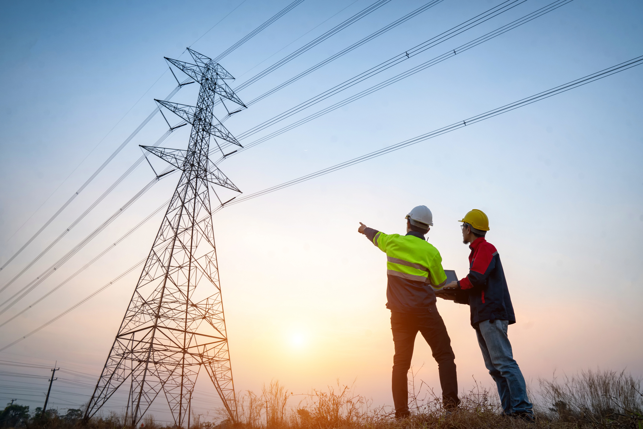 Two powerline operators point up at a high tension tower