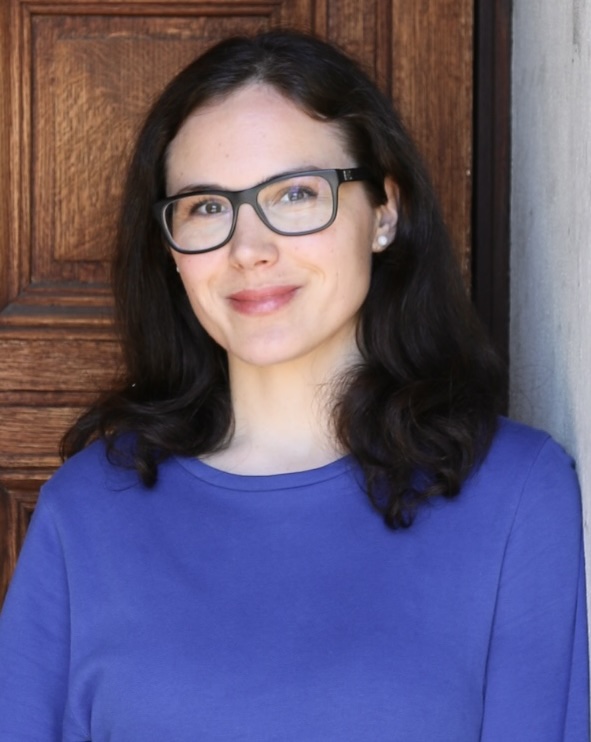 Woman with long dark hair and glasses in a purple shirt smiling in front of a door