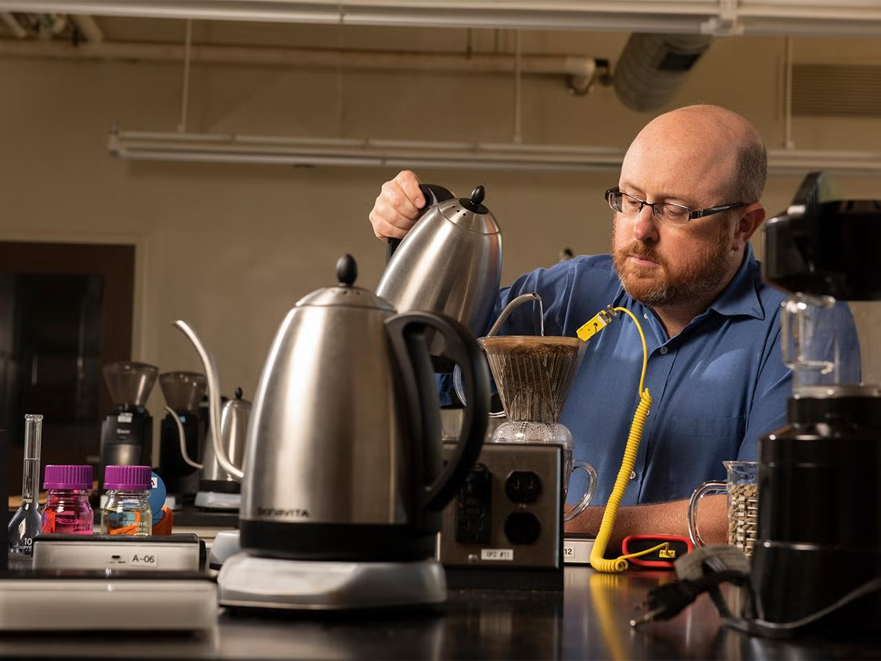 Bald man with a beard makes pour over coffee on a lab table