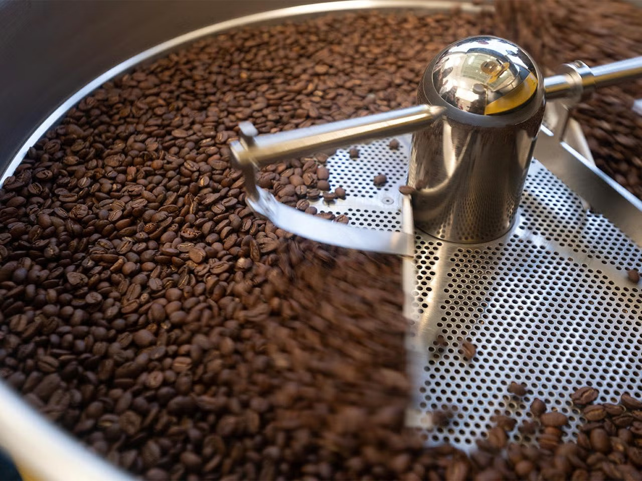 A big roaster bowl full of brown coffee beans