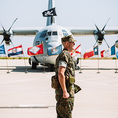 A Marine in profile with a military plane behind him and a row of flags