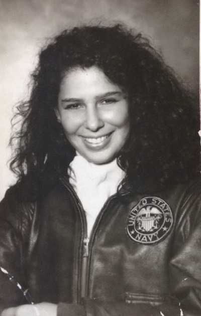 A woman with long dark curly hair smiling at the camera in a Navy leather jacket