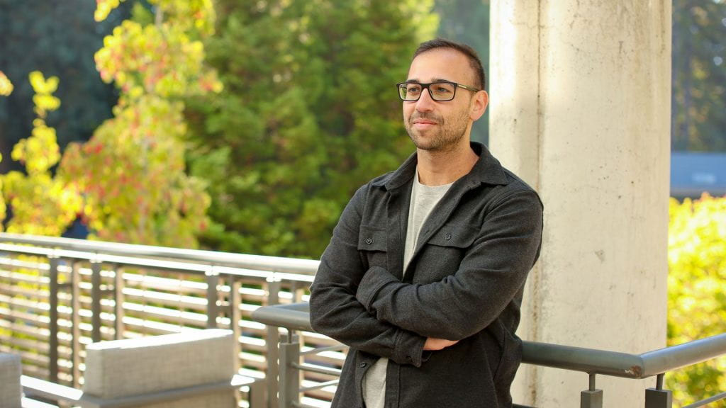 Assistant Professor of Electrical and Computer Engineering Jason Eshraghian smiles faintly, arms crossed over his chest, on a balcony