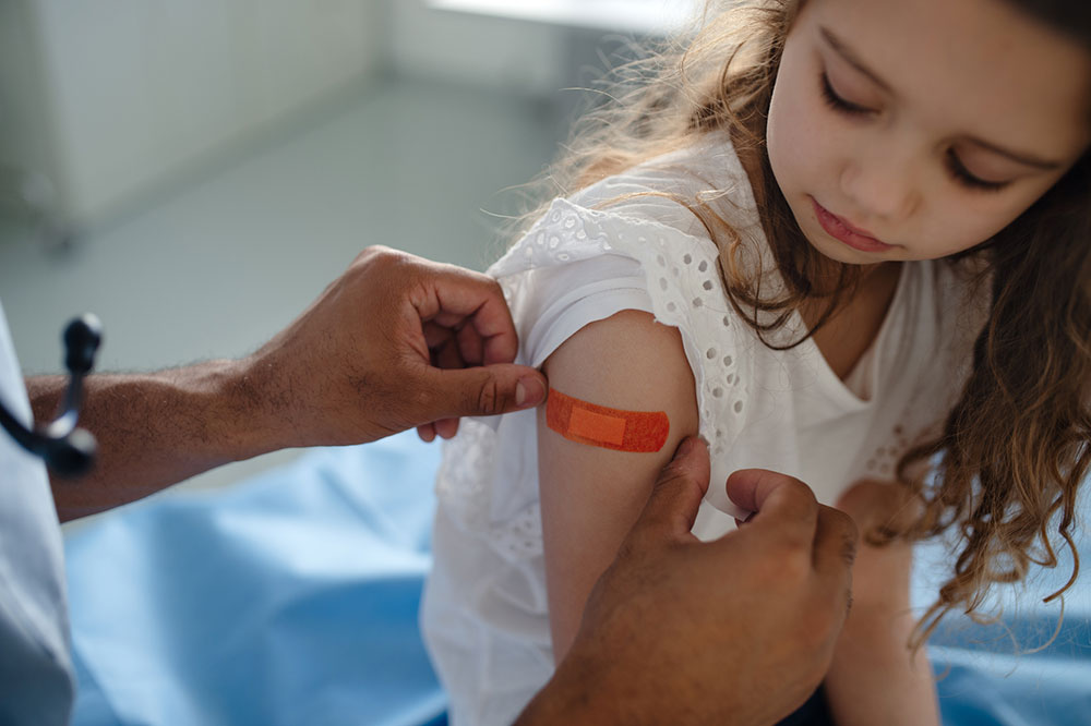 A doctor puts a bandaid on a girl's upper arm while the girl watches