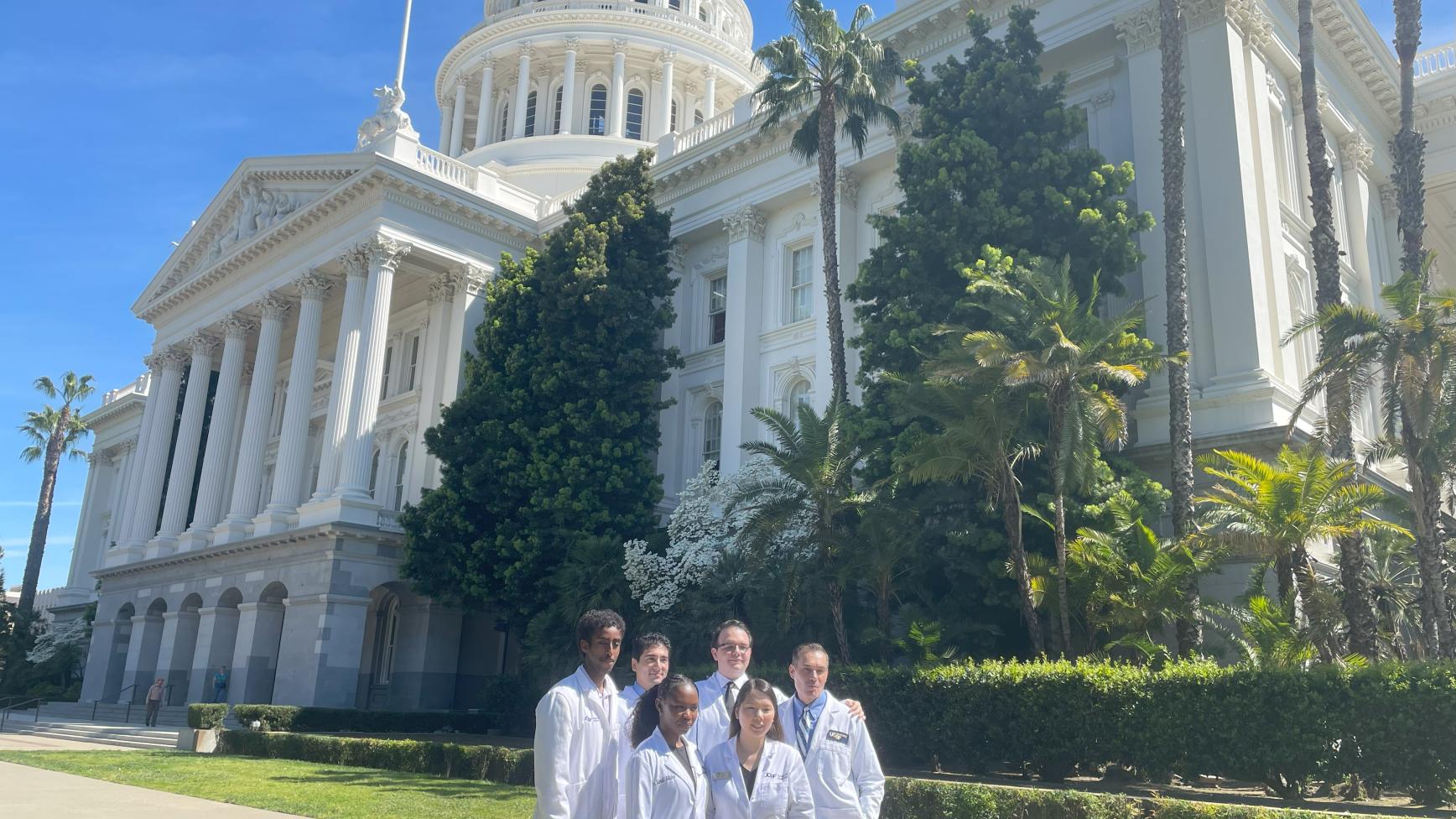 A group in white coats poses in front of the California state capitol building