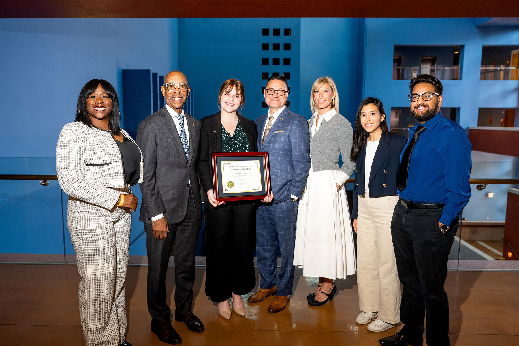 Maddison Crump holds a plaque and poses for a photograph with UC Student Regent Designate Sonya Brooks, UC President Michael Drake, UC Merced Chancellor Juan Sánchez Muñoz, UC Regent Chair Janet Reilly and UC Student Regent Josiah Beharry.  