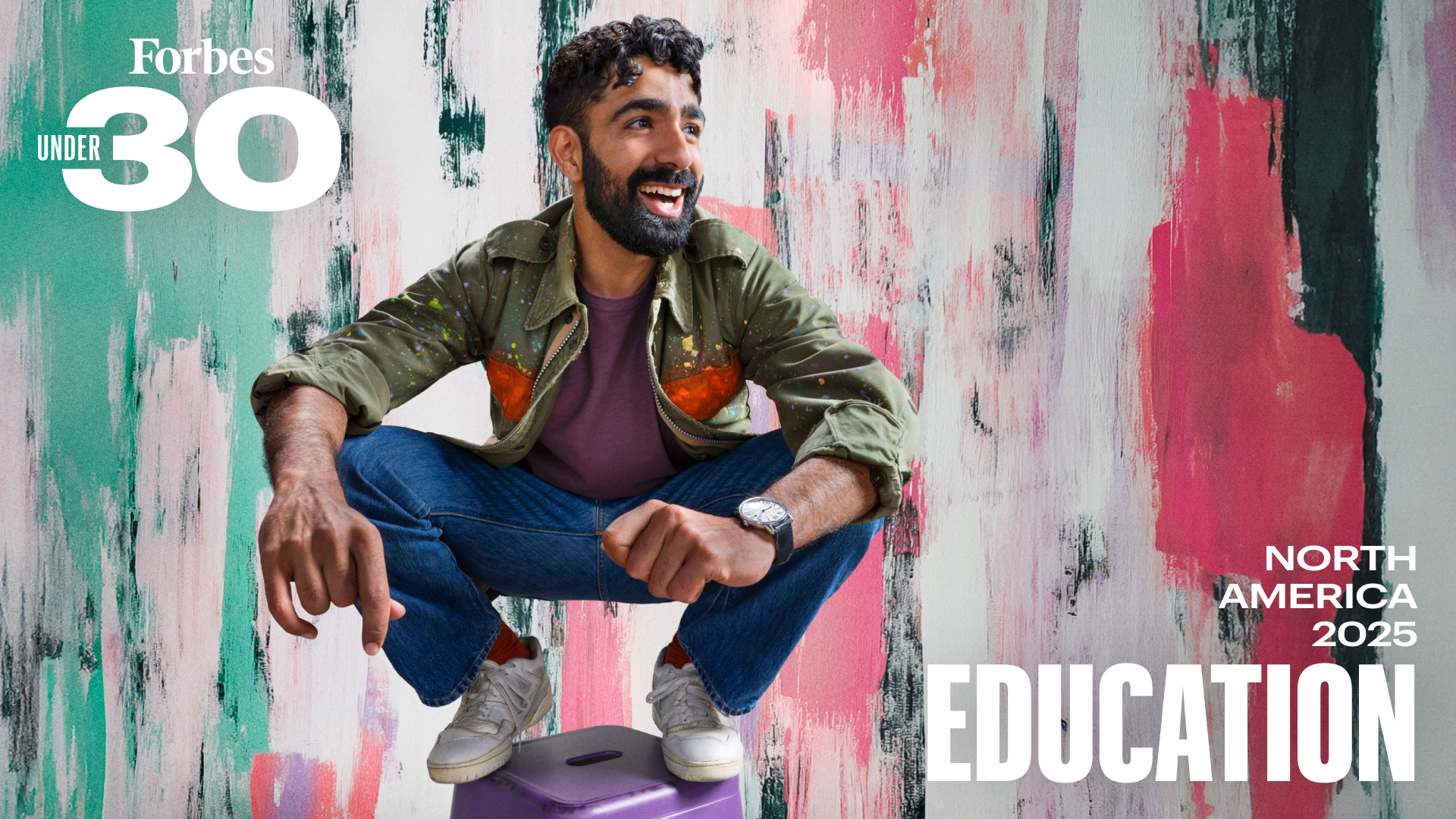 In front of a colorful background, a young man with a beard crouches on a stool and smiles enthusiastically, Forbes 30 Under 30 Education branding on the image