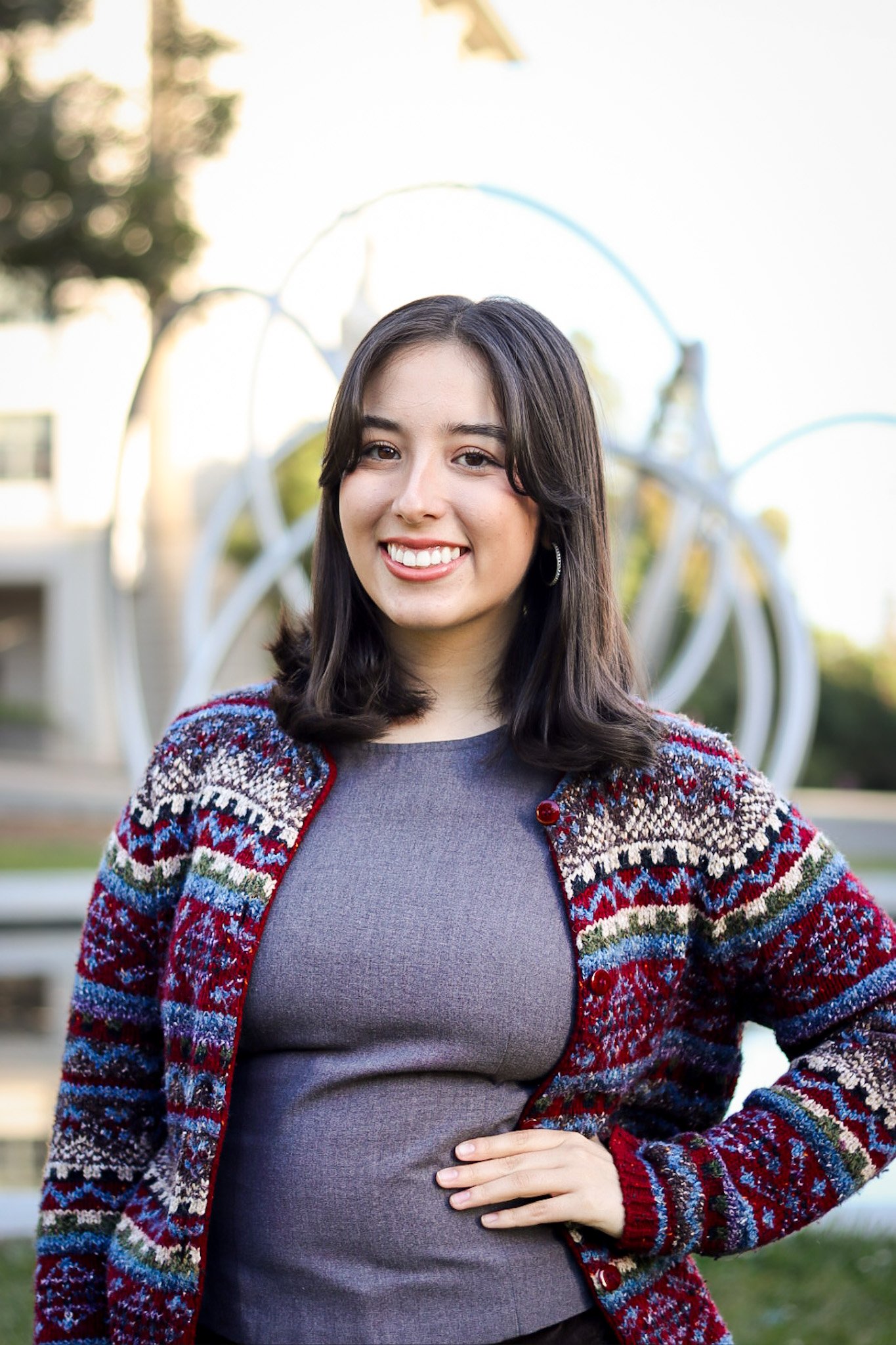 Sophia Garcia smiles for the camera in an outdoor portrait in front of a public art installation on Berkeley's campus.