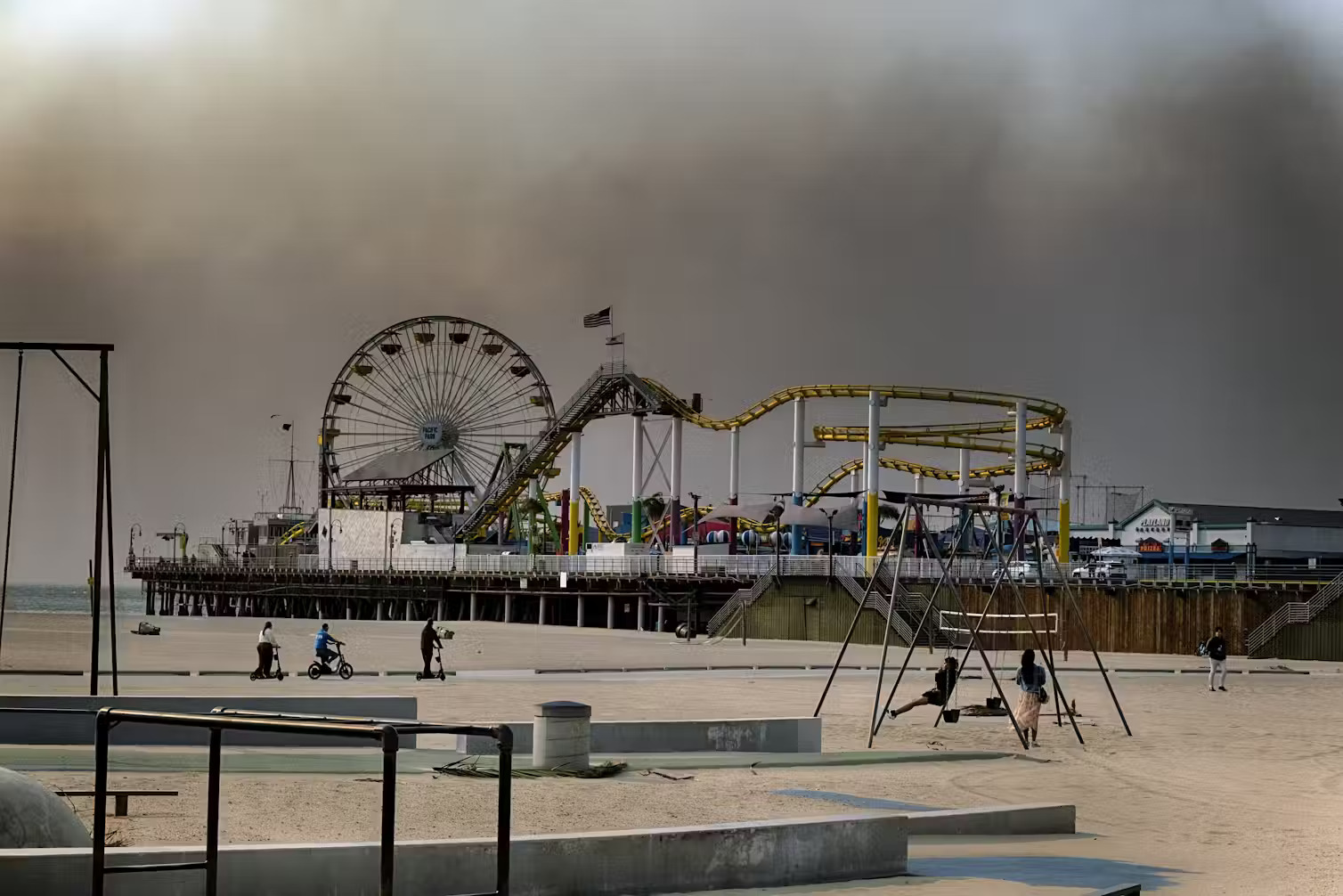 Santa Monica Pier fairgrounds, with very few people in the foreground, surrounded by aerial smoke