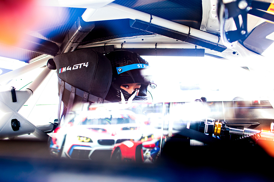 Photo of a woman in full racing gear inside a race car