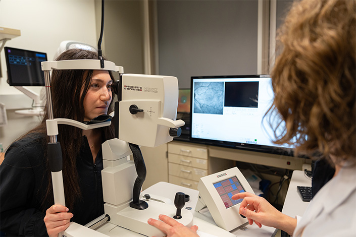 Someone with long dark hair gets their eyes examined by a doctor with wavy hair