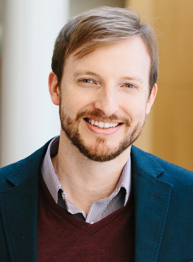 Kole Roybal, wearing a blazer and sweater, smiles in a professional headshot