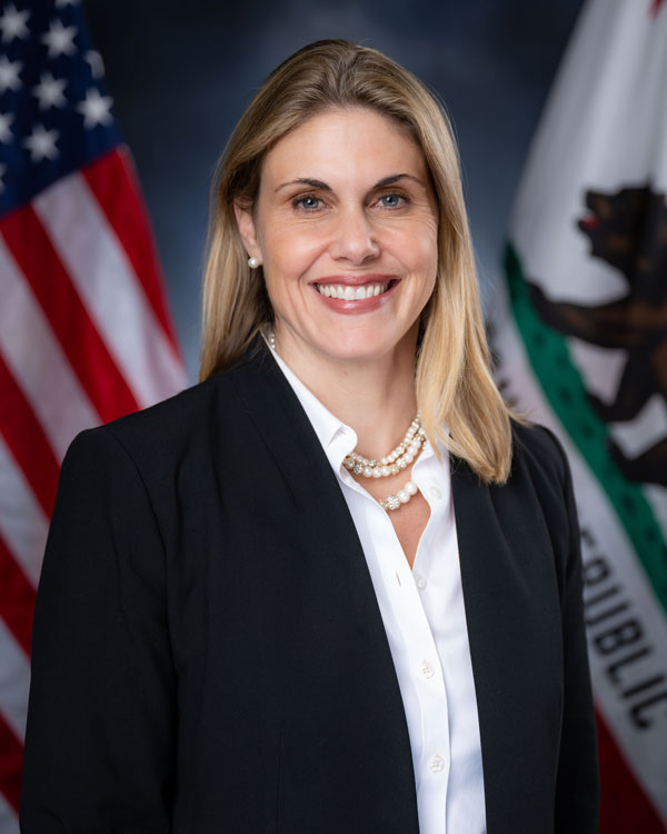 Maggy Krell smiles for an official portrait in front of the U.S. and California flags.