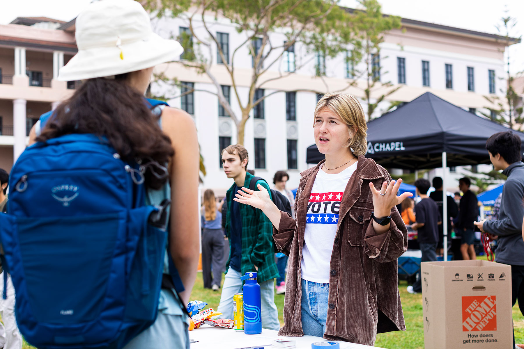 Jeanne Broome speaks with a fellow UCSB student at a voter registration booth, wearing a shirt that reads VOTE