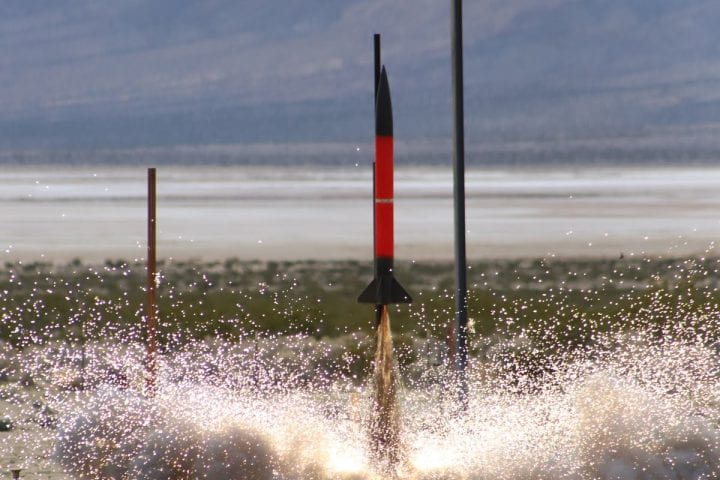 A slim black and red rocket launches in the Mojave Desert