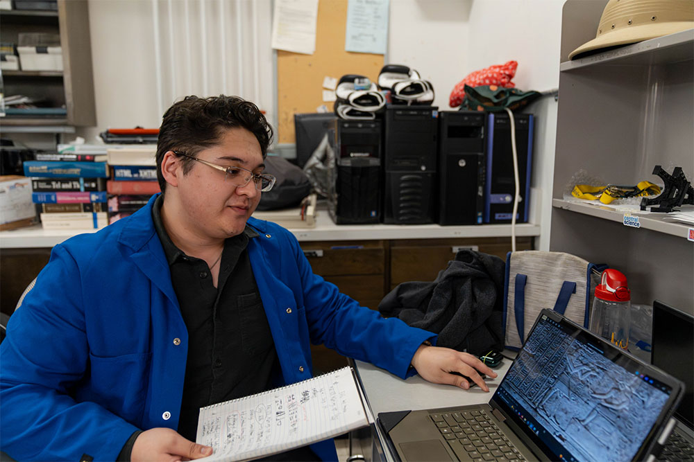 Liam McEvoy holds a notebook and types on a computer in a lab