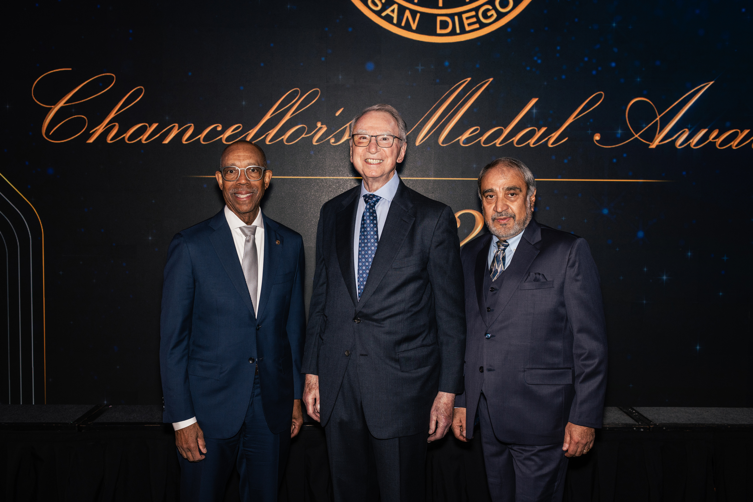 President Drake, Irwin Jacobs and UC San Diego Chancellor Pradeep Khosla stand in front of a large backdrop that says Chancellor's Medal Awards