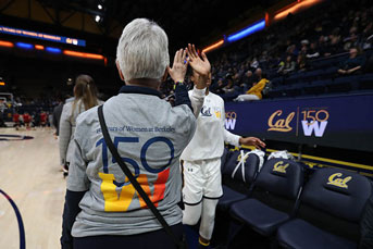 The back of a women wearing a grey t-shirt with the 150W logo faces the camera as she gives a high five to a basketball player