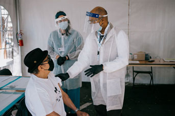 President Drake talks to a man about to receive the vaccine, woman nurse behind him