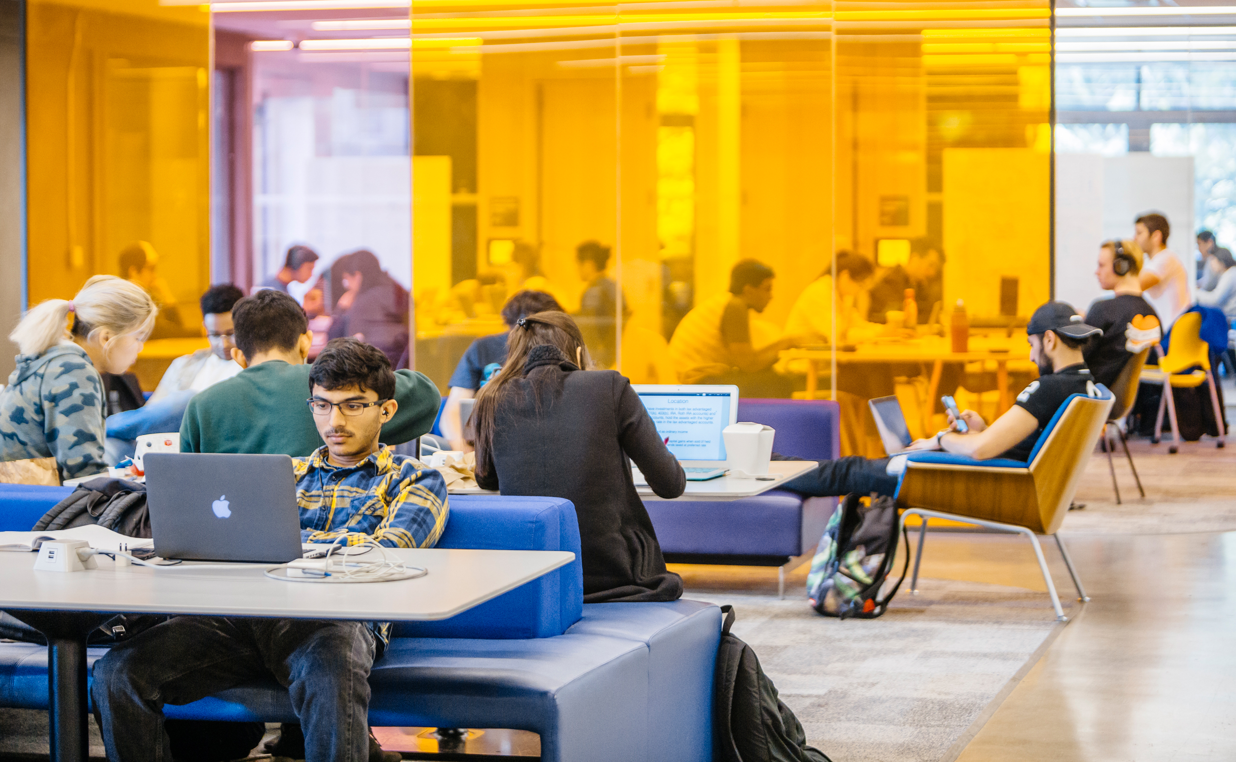 students working on laptop computers at tables in a large study space