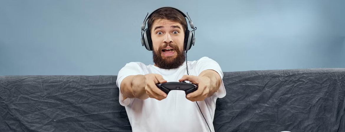 A man sitting on a couch with headphones on holding a video game controller with a surprised, frightened expression