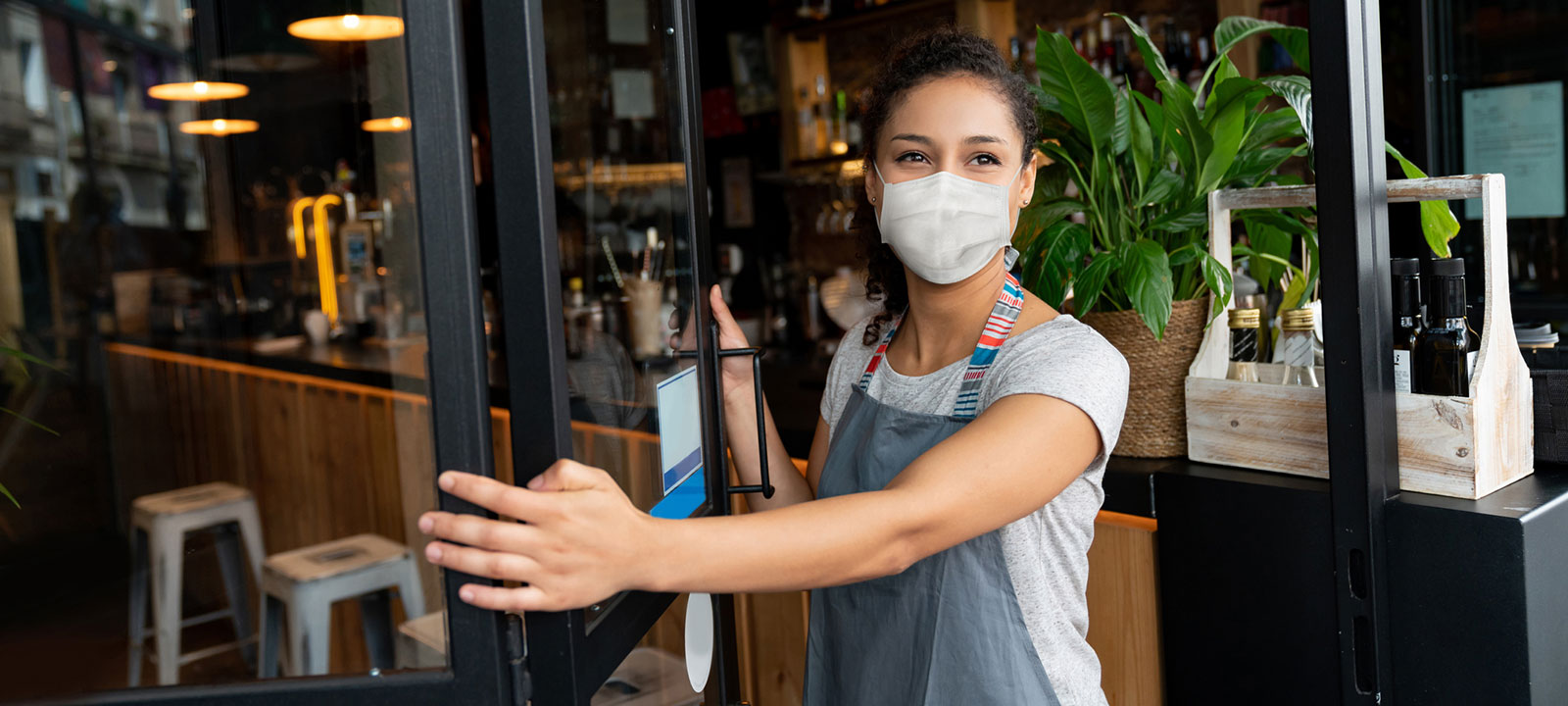 Woman wearing mask opens a cafe door