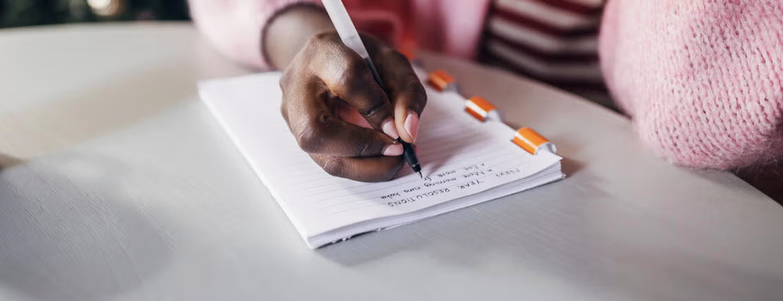 A close-up of a hand holding a pen writing a list in a notebook