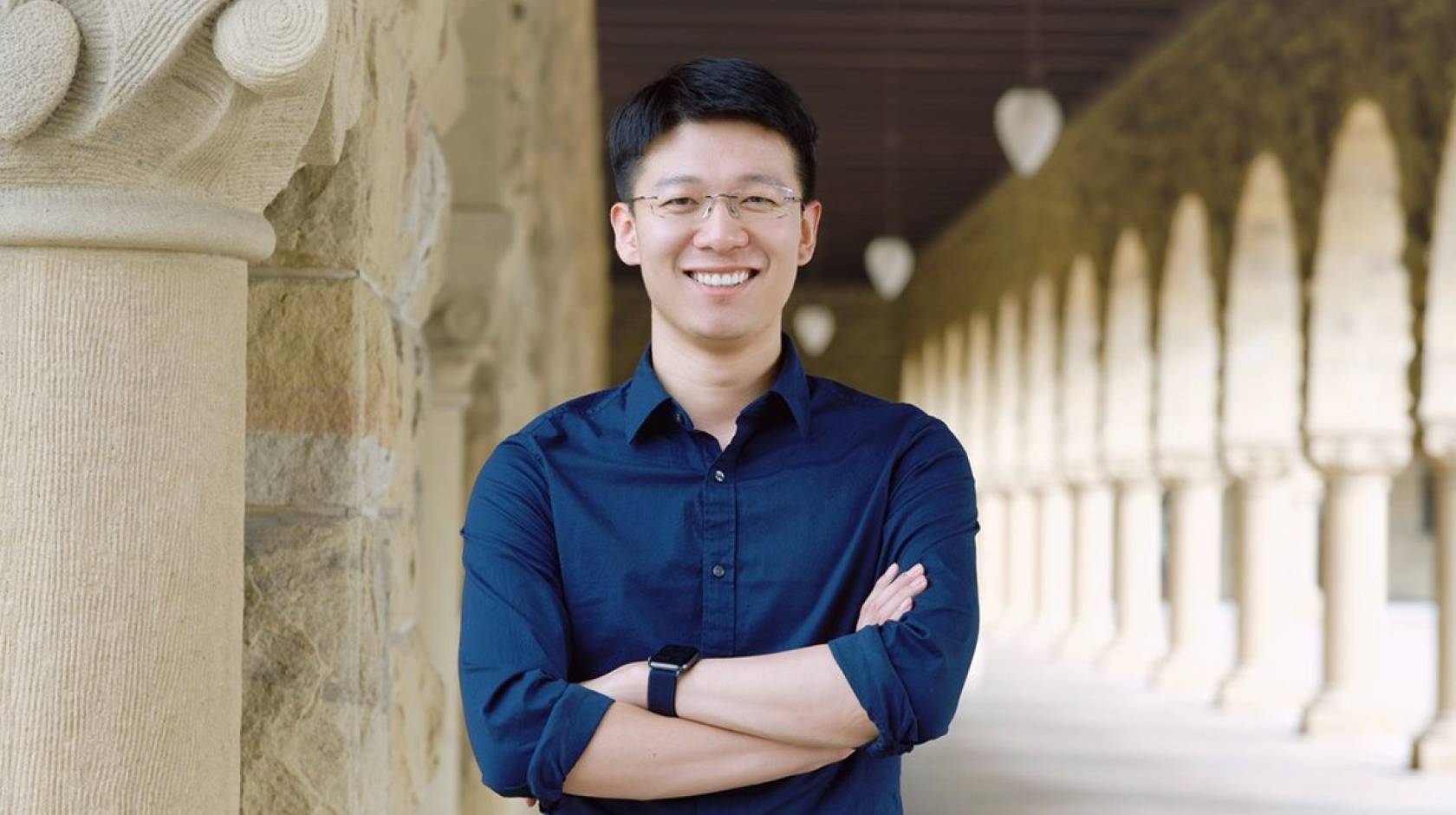 A person standing with crossed arms and smiling in front of a colonnade 