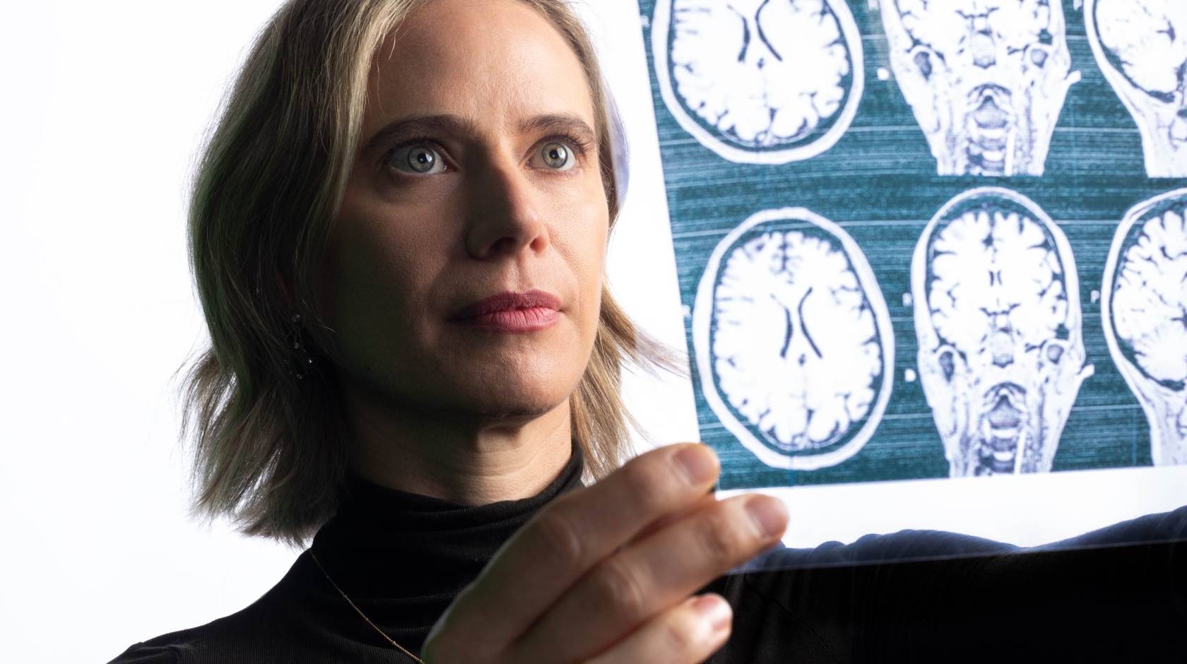 A woman holds a sheet of negatives showing scans of brains up to the light