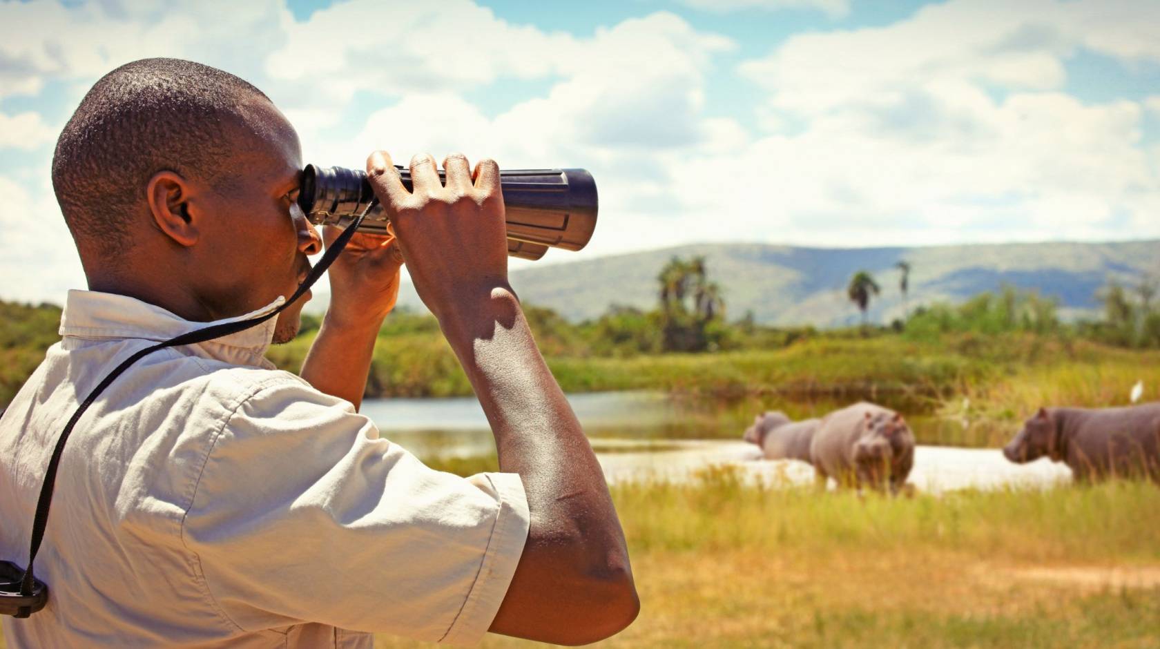 A man in profile looks through binoculars while standing in a field