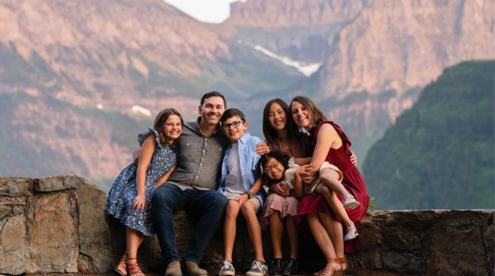 The Finlayson family, a man, woman and 4 kids, poses for a photograph in front of a mountain landscape.