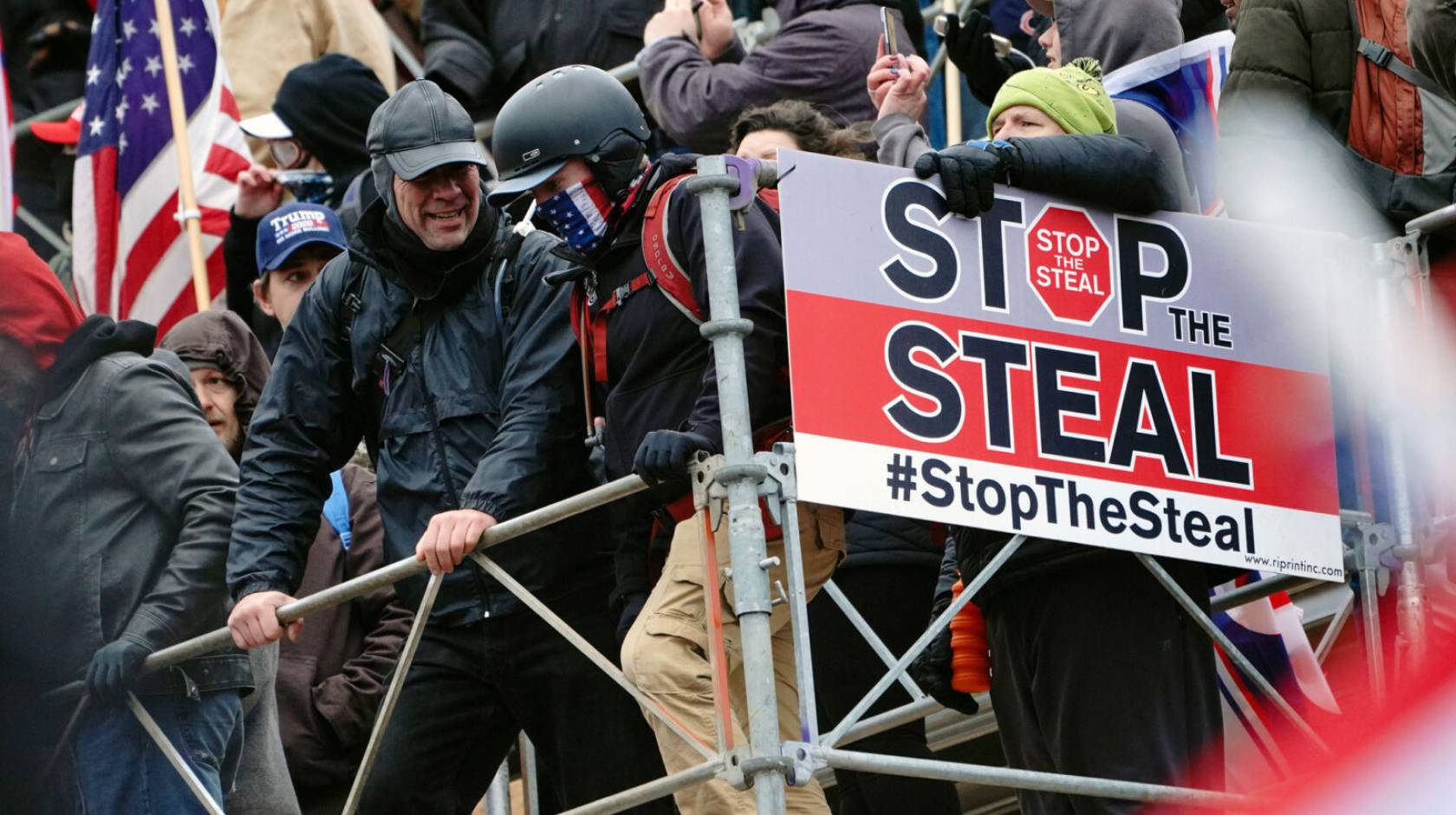 People wearing tactical gear attack the Capitol on Jan 6th, with a big sign reading "Stop the Steal"