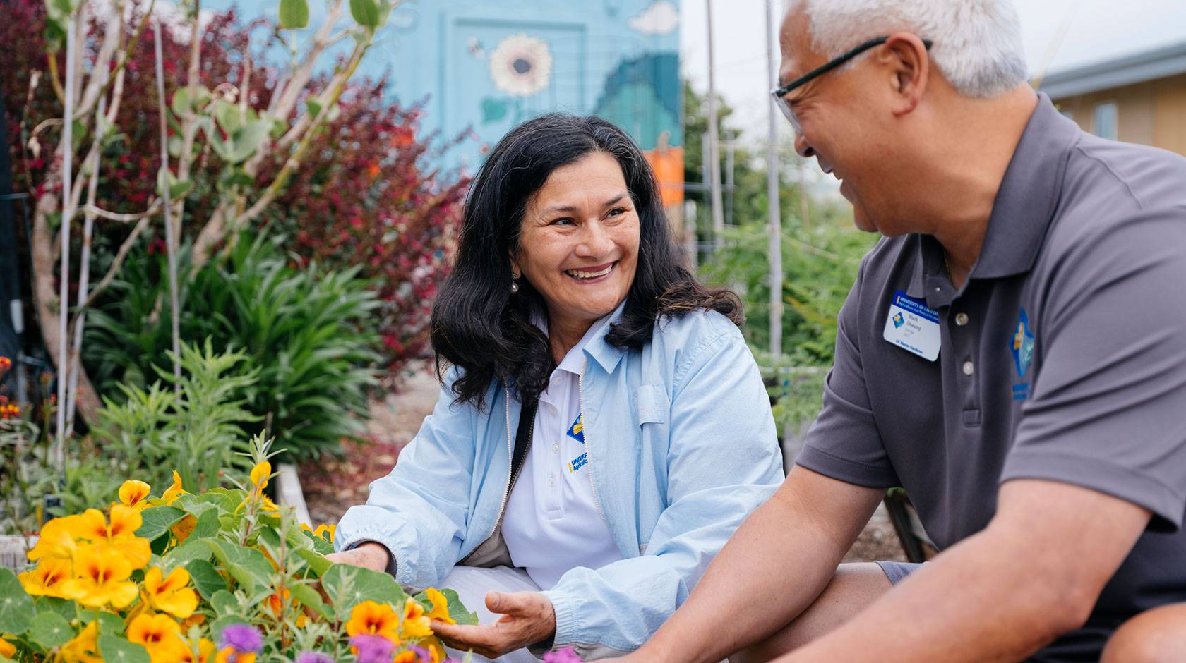 A man and woman smile while tending to a colorful garden.