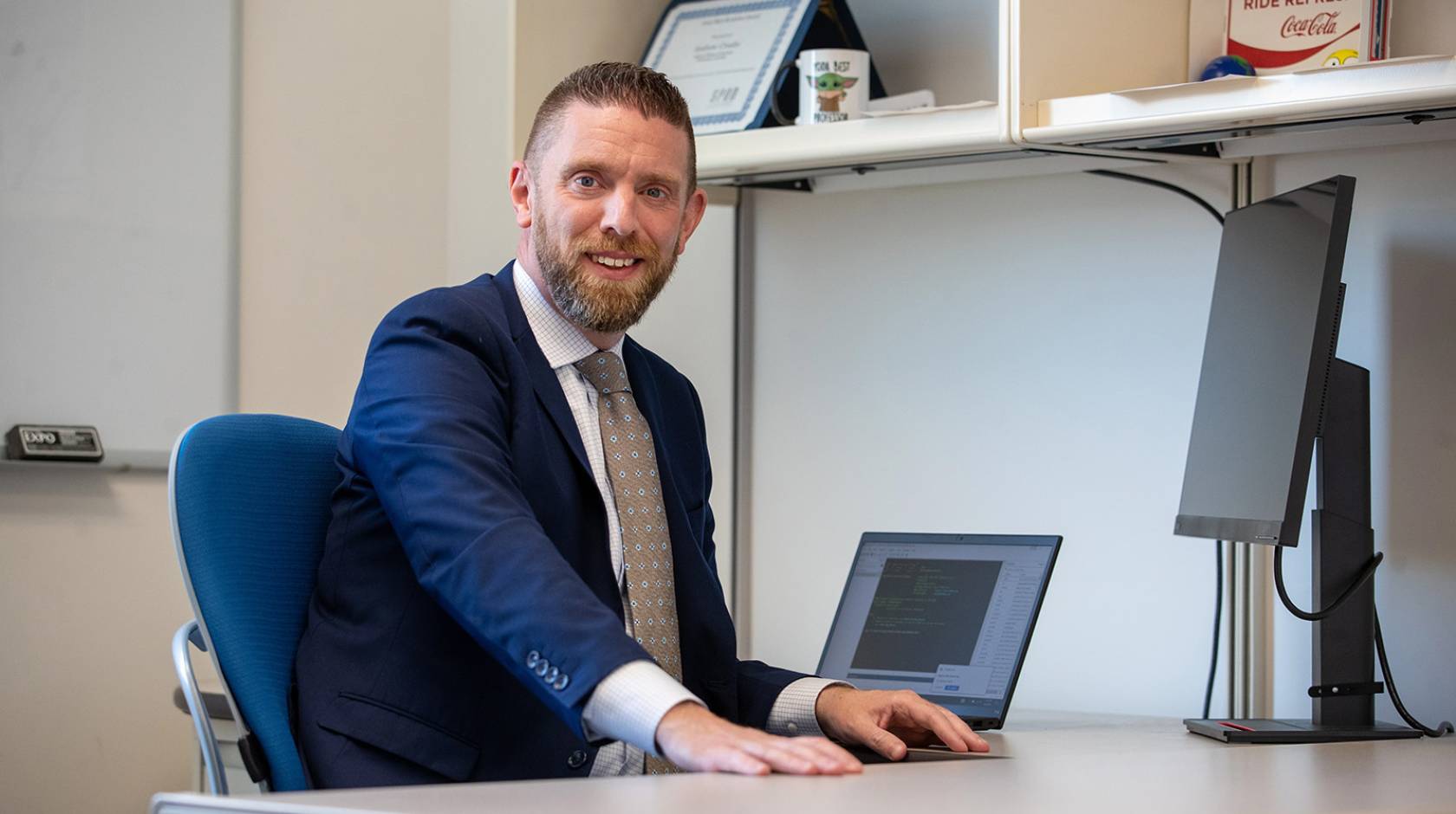 Andy Crosby at his desk, smiling at the camera, wearing a blue suit