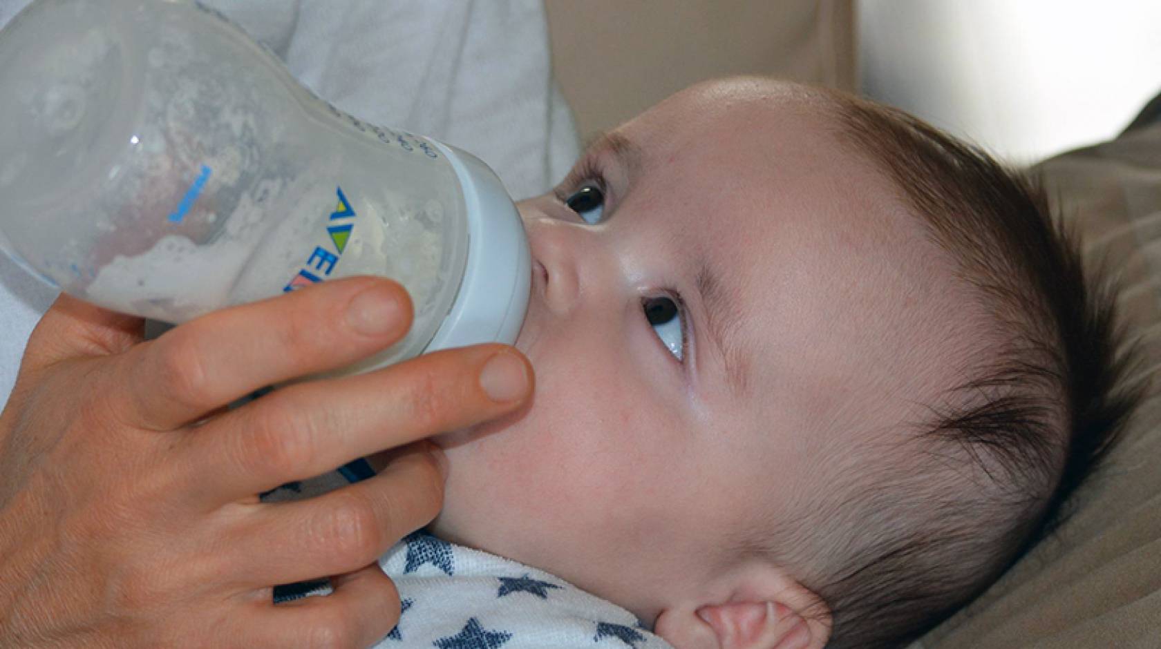 Baby drinking from a bottle looking up at person feeding