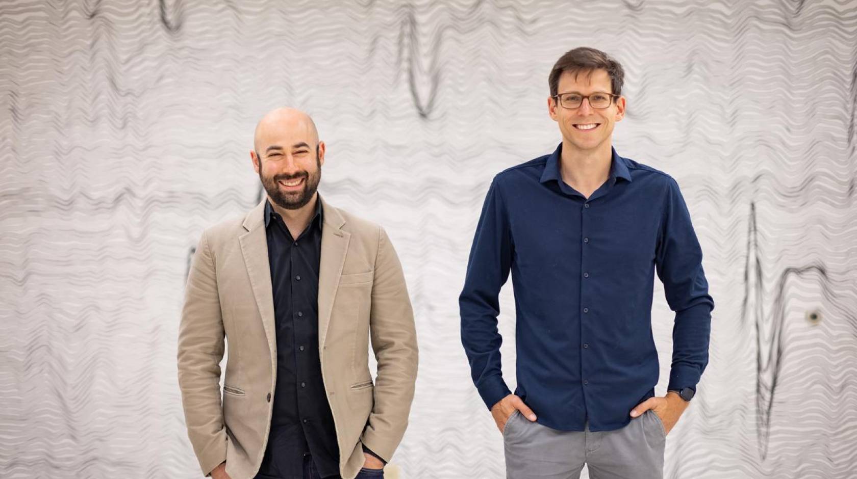 Two men standing together in front of a backdrop of wavy lines